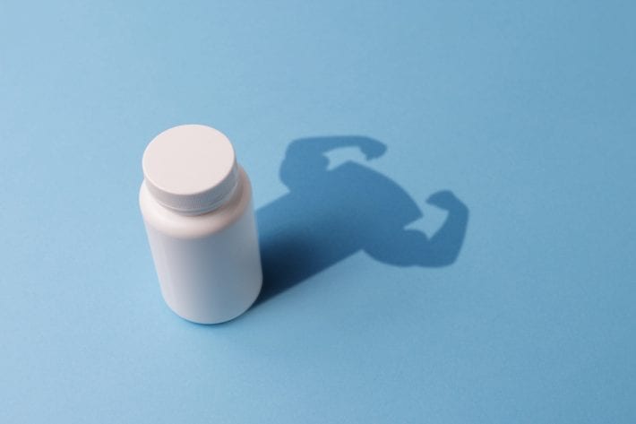Plastic Bottle with Tablets and the Shadow with the Hands of the Bodybuilder. Concept of Steroids and Pharmaceutical Preparations for Bodybuilders. Pharmaceutical Preparations for rapid muscle growth